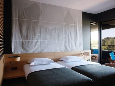Moderner Hotelzimmer mit zwei Betten, großen Fenstern und Balkon mit Ausblick auf die Natur.