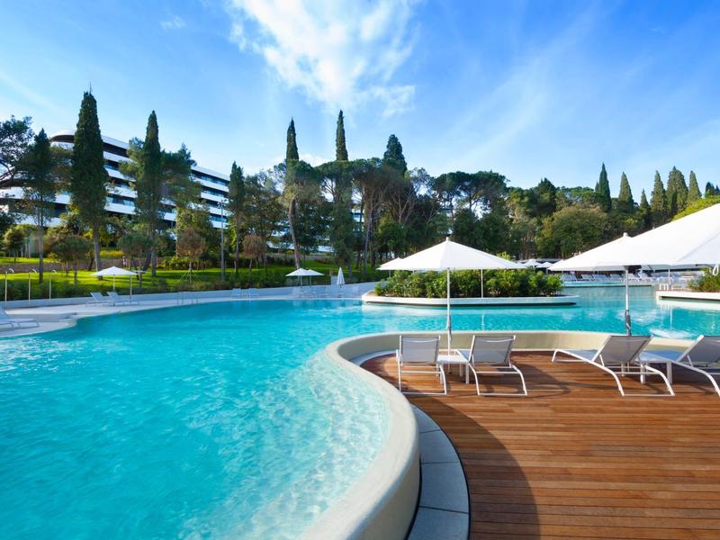 Zapraszający basen na świeżym powietrzu z leżakami i parasolami na tle zielonego parku.