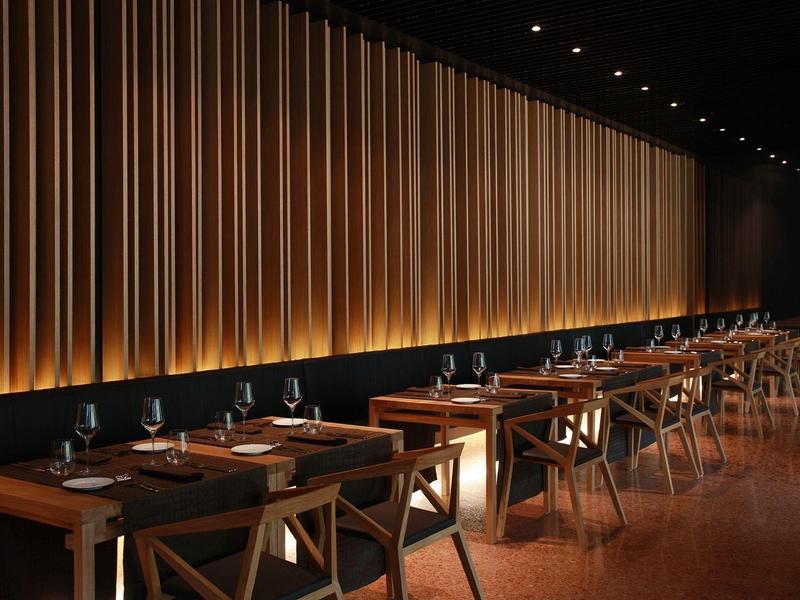 Nowoczesna restauracja z drewnianymi krzesłami i ciepłym, pośrednim oświetleniem na ścianie.