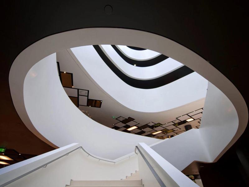Widok w górę na nowoczesne, zakrzywione schody z białymi ścianami i szklanym poręczem.