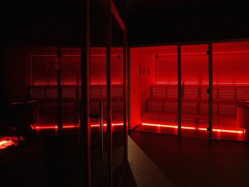 Ciemne pomieszczenie z czerwonym oświetleniem LED i szklanymi ścianami, prawdopodobnie nowoczesna strefa spa.
