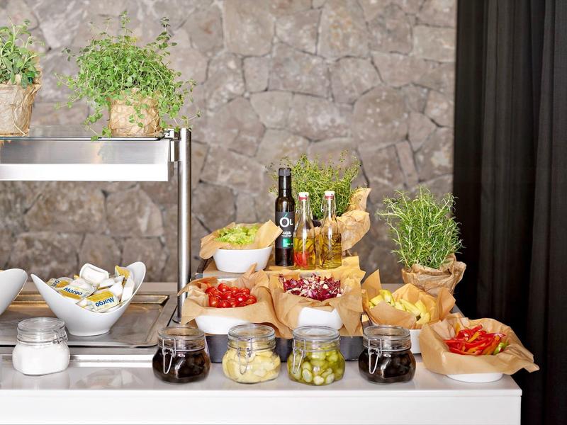 Bufet z różnymi marynowanymi potrawami i ziołami na tle kamiennej ściany w hotelu.