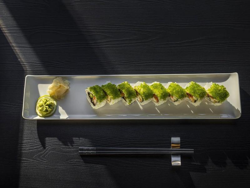 Długi biały talerz z rzędem sushi i wasabi, na ciemnym stole z pałeczkami.