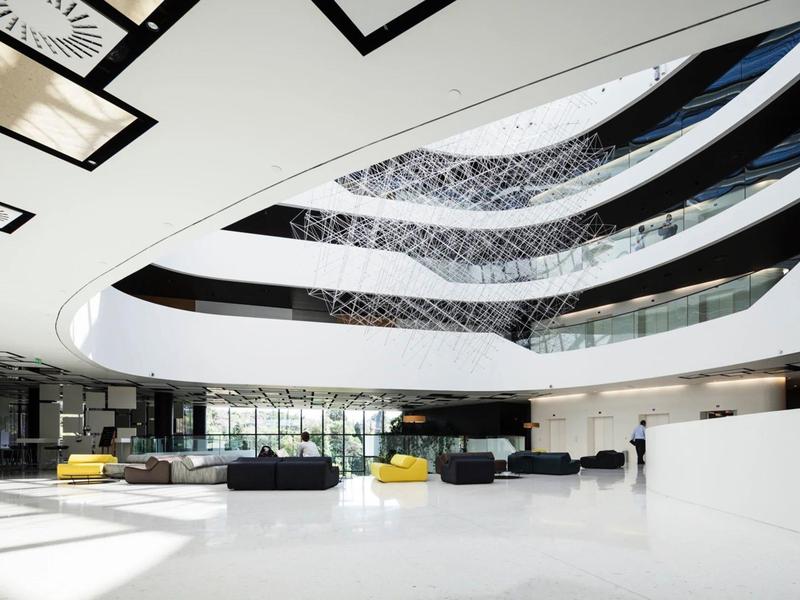 Przestronne nowoczesne lobby hotelowe z białą podłogą, zakrzywionym oknem sufitowym i miejscami do siedzenia.