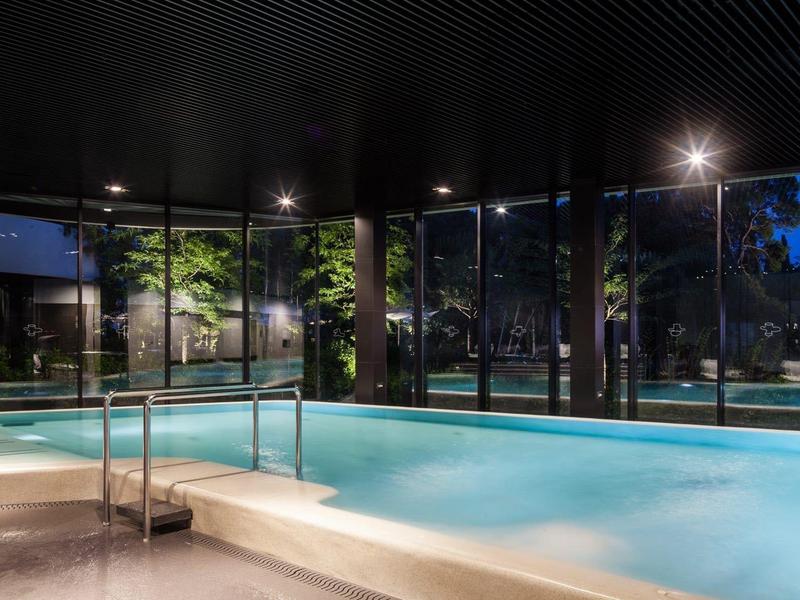 Basen kryty z dużymi panoramicznymi oknami i widokiem na drzewa o zmierzchu.