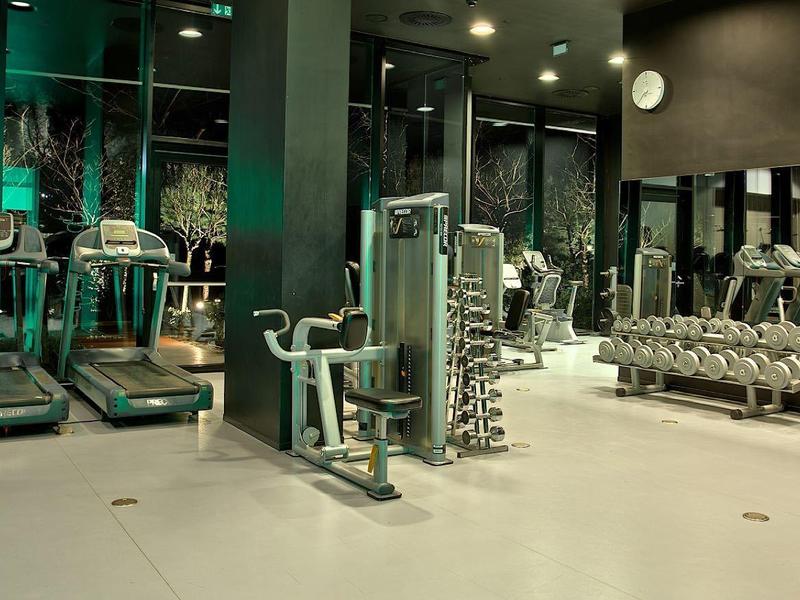 Nowoczesna siłownia z różnymi urządzeniami do ćwiczeń i hantlami w jasnym pomieszczeniu.