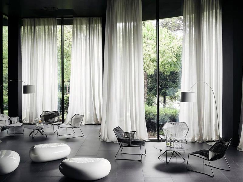 Nowoczesny, minimalistyczny salon z dużymi oknami i białymi zasłonami.