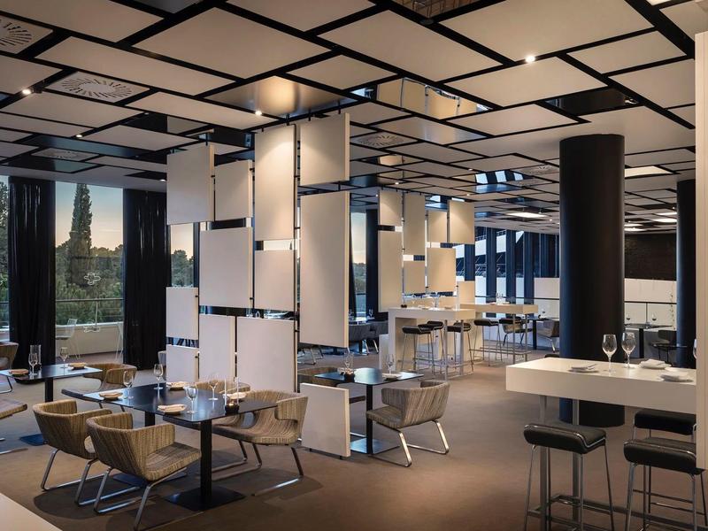 Nowoczesna restauracja z eleganckim wystrojem i panoramicznymi oknami z widokiem na zieleń.