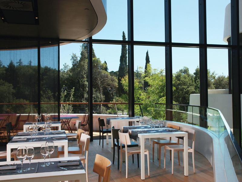 Wnętrze restauracji z dużymi oknami i widokiem na zielone drzewa.