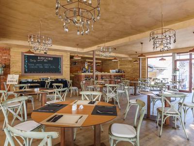 Helles Restaurant mit Holztischen, weißen Stühlen und Kronleuchtern unter einer Holzdecke.