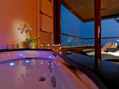 Whirlpool auf Balkon mit Blick auf beleuchtete Stadt bei Nacht neben Liegestühlen.