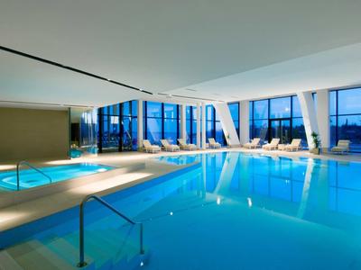 Vnitřní bazén s velkými okny a lehátky v moderním hotelu