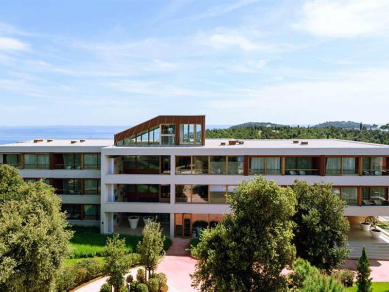 Moderní vícepodlažní hotelová budova se zahradou a výhledem na moře pod modrou oblohou.