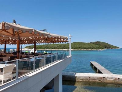 Terasa restaurace u moře s deštníky s výhledem na mol a kopce.