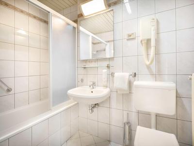 Kompaktes Badezimmer mit Badewanne, Waschbecken, Toilette und Wandföhn in weißen Fliesen.