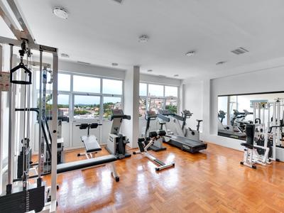 Heller Fitnessraum mit großen Fenstern und modernen Trainingsgeräten mit Blick auf die Stadt.