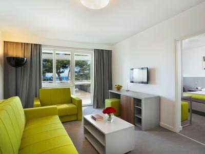 Modernes Wohnzimmer mit grünem Sofa, TV an der Wand und Blick auf Balkon mit Bäumen.