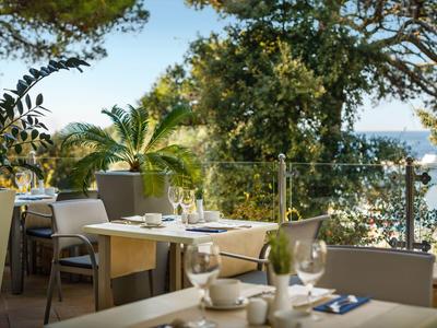 Terrasse mit gedeckten Tischen und Blick auf das Meer, umgeben von grünen Bäumen.