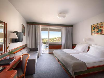 Modernes Hotelzimmer mit Doppelbett, Schreibtisch und Balkon mit Aussicht auf die Stadt.