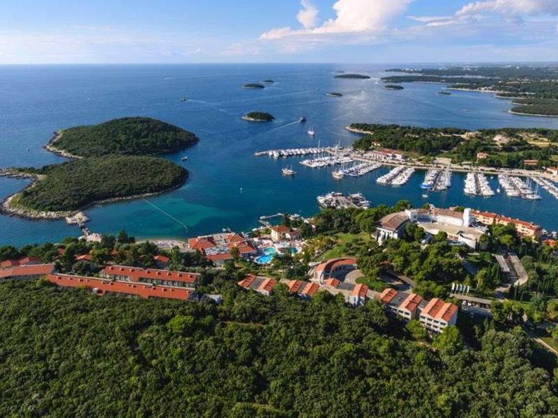 Letecký pohled na pobřežní město s přístavem, jachtami a zalesněnými ostrovy.