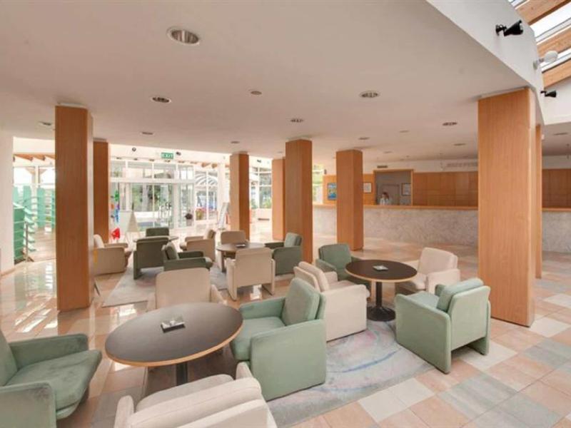 Světlá hotelová lounge s posezením a stoly na dlažbě.