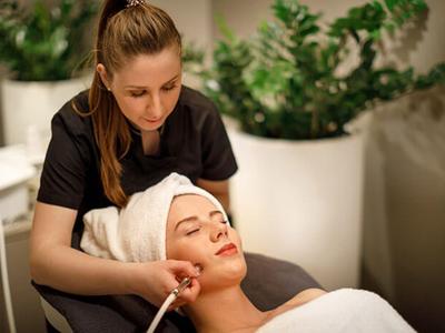 Žena dostává obličejovou masáž ve spa, obklopena relaxační atmosférou a rostlinami.