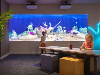Des enfants jouent dans une pièce avec un grand aquarium lumineux sur le mur.