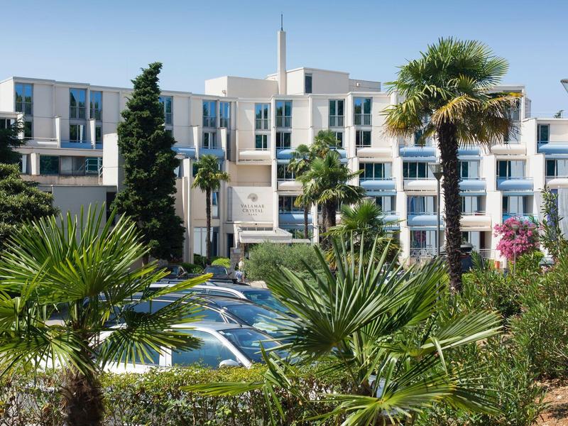 Complexe hôtelier blanc moderne avec piscine et palmiers au premier plan sous un ciel bleu.