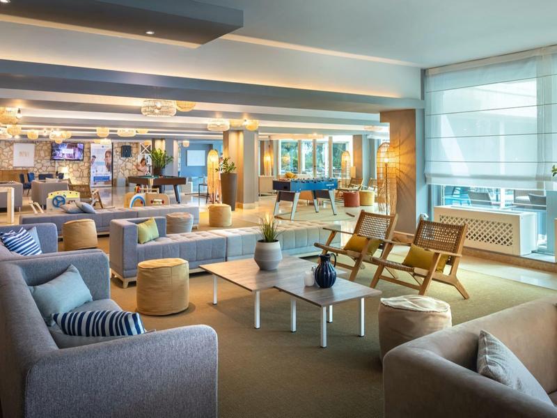 Un salon d'hôtel moderne avec canapés, fauteuils, tables basses en verre et grandes fenêtres.