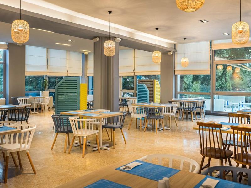 Salle à manger moderne avec tables en bois, chaises et lampes suspendues dans un restaurant lumineux.
