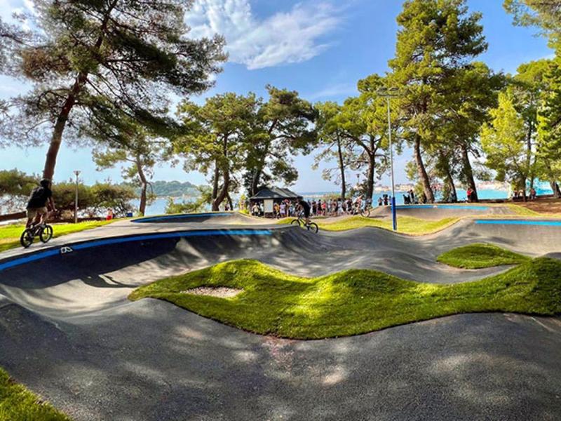 Une piste de BMX extérieure sinueuse entourée d'arbres sous un ciel bleu.