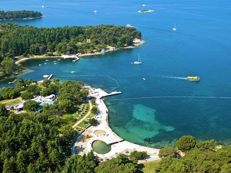 Vue aérienne d'un littoral boisé avec eau claire et petites plages.
