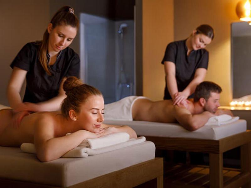 Deux personnes reçoivent un massage du dos dans une salle de spa calme avec un éclairage doux.