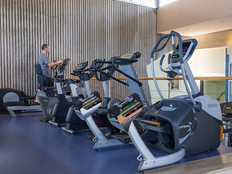 Équipements de fitness modernes comme vélos d'appartement et elliptiques dans une salle lumineuse et propre.
