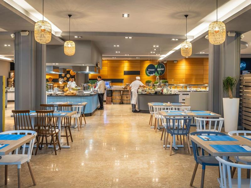 Restaurant moderne avec chaises bleues, tables en bois et lumière chaude dans un hôtel.