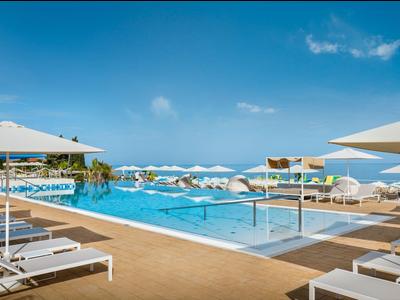 Modern pool area with white lounge chairs and umbrellas under a blue sky.