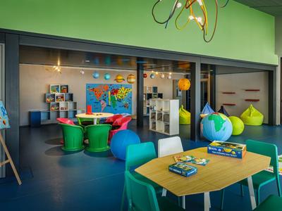 Área de juegos para niños colorida con pufs, mesas, materiales educativos y mapas en la pared.