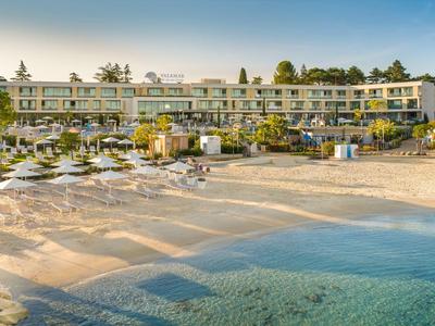 Strand mit Sonnenschirmen, klarem Wasser und mehrstöckigem Hotel im Hintergrund bei Sonnenlicht.