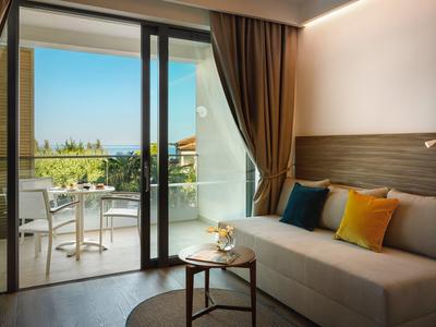 Habitación de hotel acogedora con sofá y balcón con mesa y sillas, vista al jardín.