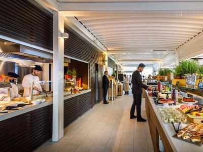 Área de desayuno moderna en hotel con buffet y huéspedes en ambiente relajado.