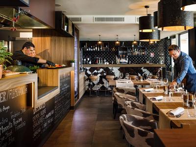 Modern restaurant with wooden tables and cozy lighting, two people preparing the space.
