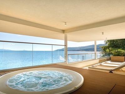 Hot tub on a terrace with sea view and two lounge chairs beside it.