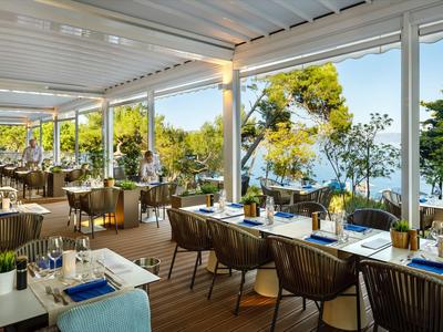 Open-air restaurant with sea view, blue sky, and green scenery in daylight.