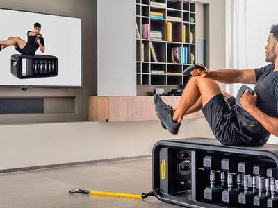 Man exercises with dumbbells in front of a TV in a modern living room.