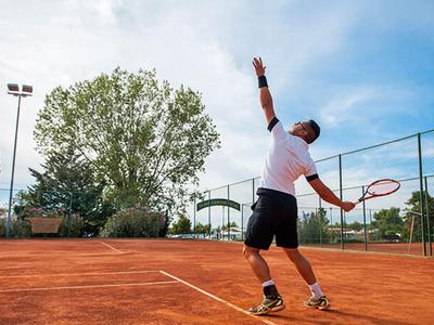 Man playing tennis on an outdoor red clay court in daylight.