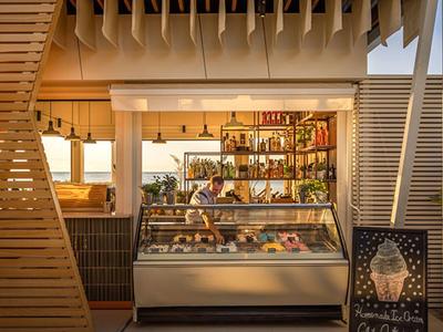 Área de bar de hotel moderno con decoración tiki, barra iluminada y revestimiento de madera exterior.