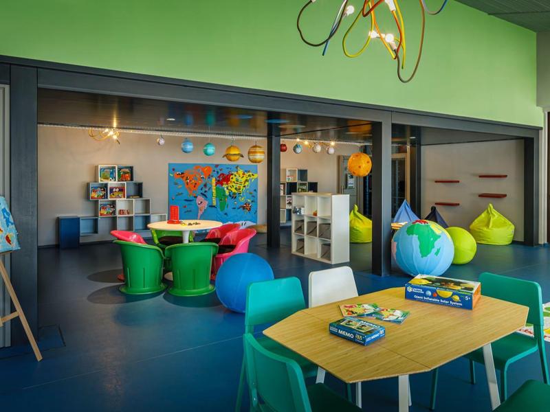 Área de juegos para niños colorida con pufs, mesas, materiales educativos y mapas en la pared.