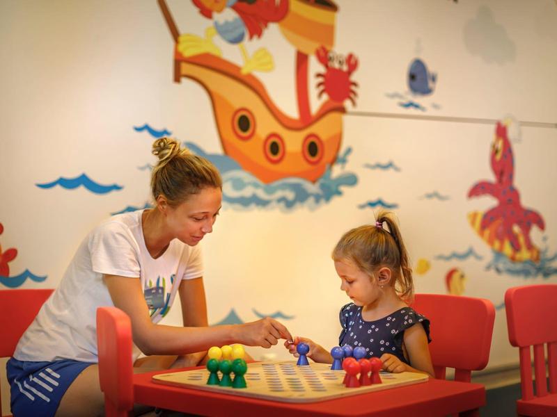 Madre e hija juegan juntas en una mesa infantil con sillas rojas frente a una pared colorida.