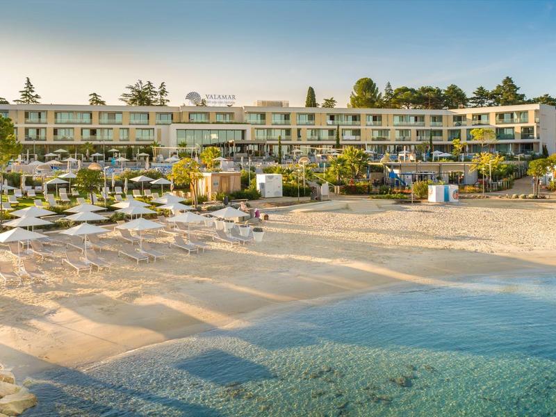 Hotel de playa con tumbonas, sombrillas y mar azul claro bajo un cielo azul.
