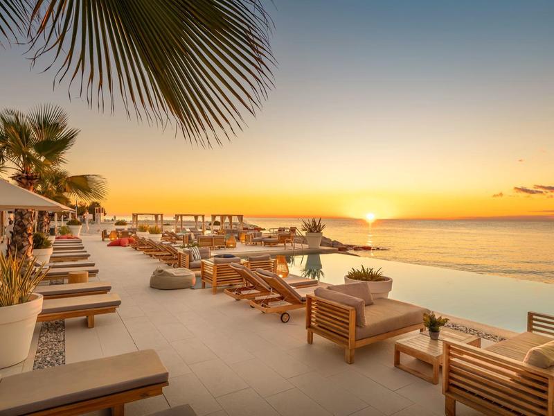 Terraza de piscina lujosa con tumbonas y vista al atardecer sobre el mar.